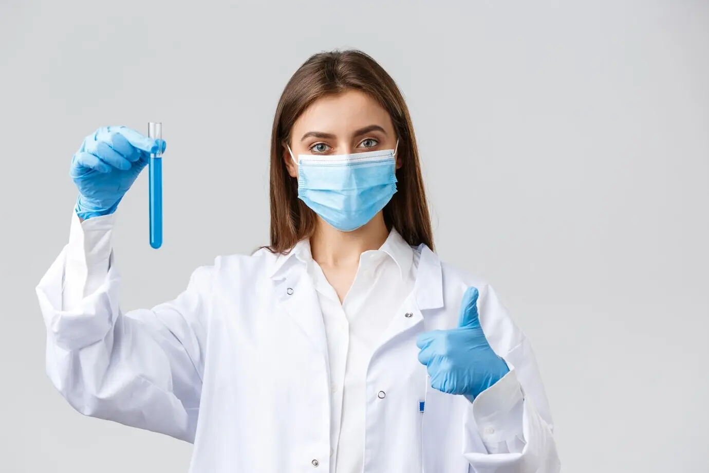 COVID‑19: концепция профилактики вируса, медицинских работников и карантина. Врач завершил тестирование вакцины от коронавируса, держит пробирку с образцом и одобряет результат, показывая большой палец вверх в знак гарантии качества.